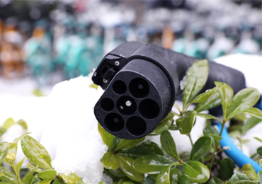 Close-up of a BESEN EV charging plug placed on snow-covered greenery, emphasizing sustainability.
