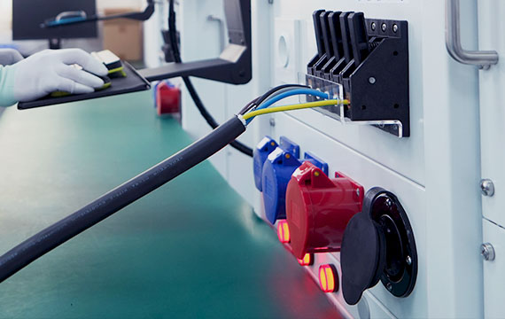 A gloved hand performing quality control tests on BESEN electric vehicle charging cables connected to a testing unit with various colored sockets.