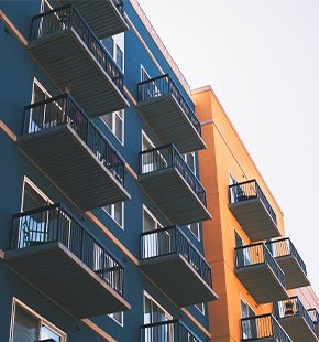 Modern multifamily housing building with blue and orange exteriors, featuring balconies on each floor.
