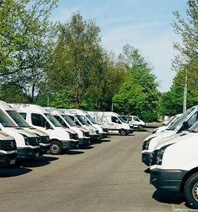 Fleet of white vans parked in an outdoor lot surrounded by trees and greenery.