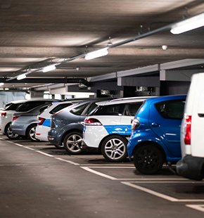 Underground parking lot with multiple parked cars, including a blue electric vehicle and a white van, under fluorescent lighting.