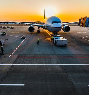 Airplane at an airport gate during sunset, with ground crew and equipment visible on the tarmac.