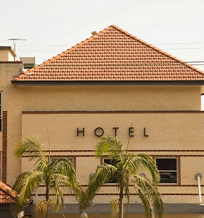 Front view of a hotel building with a red-tiled roof and palm trees, with