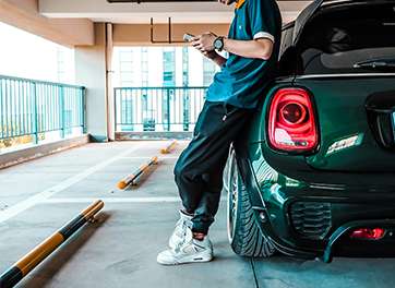 A person leaning against a green car in a parking garage, using a smartphone to perform wireless firmware updates on an electric vehicle charger.