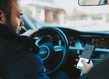 A man sitting in a car, using a smartphone to monitor the electric vehicle charger in real-time.
