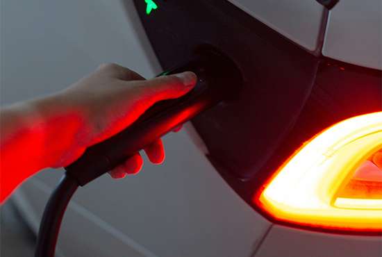 Hand plugging a charging cable into a Tesla Model 3 with the car's rear light illuminated
