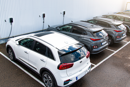 Several electric cars parked in a lot, connected to BESEN 22 kW electric car chargers mounted on a white wall.