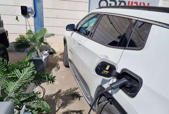White electric vehicle being charged using a BESEN EV charging station at a hotel parking area, flanked by potted plants.