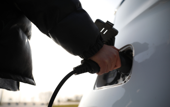 A person plugging in a BESEN GB/T plug into an electric vehicle (EV) charging port. The EV is white, and the image focuses on the connection of the charger.