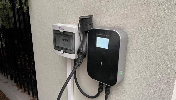 Wall-mounted BESEN Level 2 EV charger with power cables connected, installed outdoors against a white wall.
