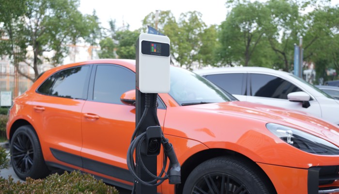 BESEN SQ20 tethered EV charger with cable attached to a charging station next to a bright orange electric SUV.