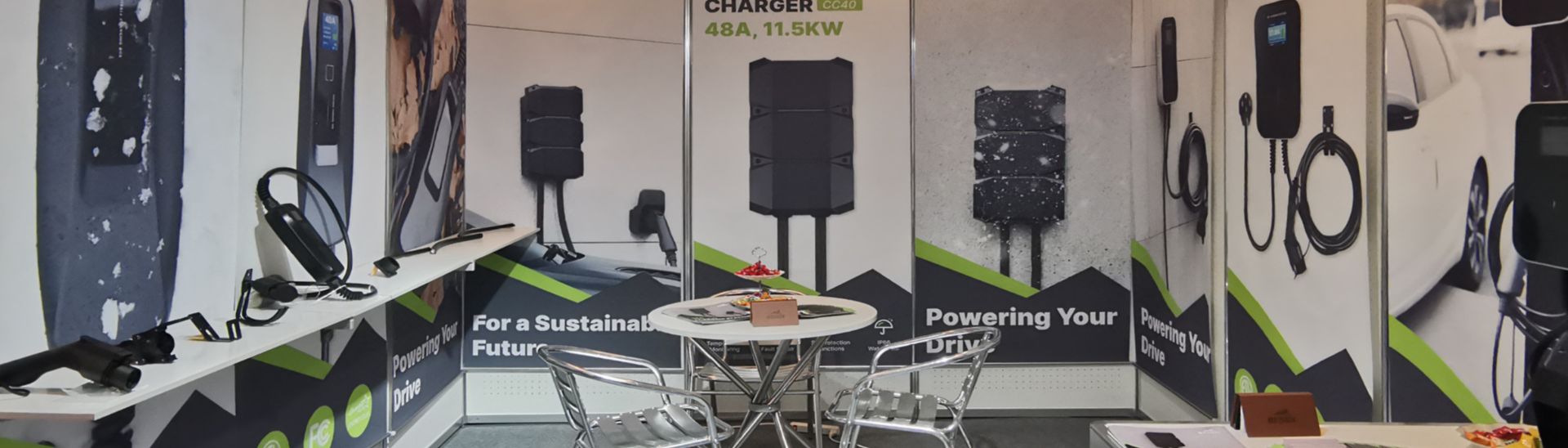 Exhibition booth displaying BESEN EV charging products, including wall-mounted chargers, portable chargers, charging cables, and a small table with chairs.