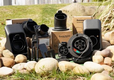 EV charging installation accessories, including mounting components, sockets, connectors, and cable holders displayed outdoors on a stone-bordered surface.